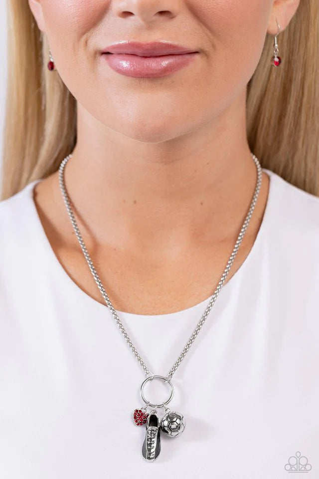 Paparazzi Accessories Corner Kick - Red Dangling from a silver hoop attached to silver popcorn chains, three soccer-inspired charms, including a silver soccer ball, black-painted cleat, and red rhinestone-encrusted heart, swing for a sporty finish. Featur