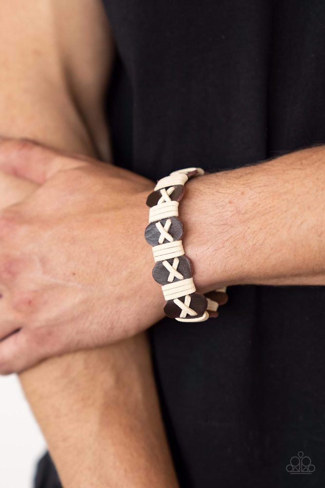 Paparazzi Accessories Macho Maverick - Brown White suede cording is threaded in a crisscross pattern along the front of a wavy brown suede band. Additional white cording wraps across the scalloped band in intervals creating a rustic handmade look. Feature