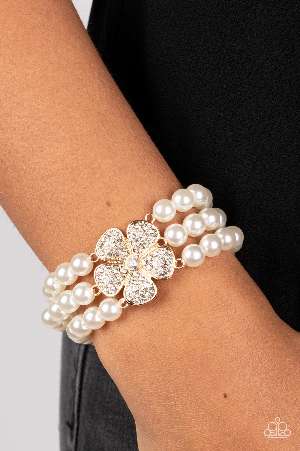 Paparazzi Accessories Park Avenue Orchard - Gold Separated by dainty gold plates, classic white pearls are threaded along three stretchy bands around the wrist. Encrusted in glassy white rhinestones, a glitzy gold flower blooms at the center of the wrist