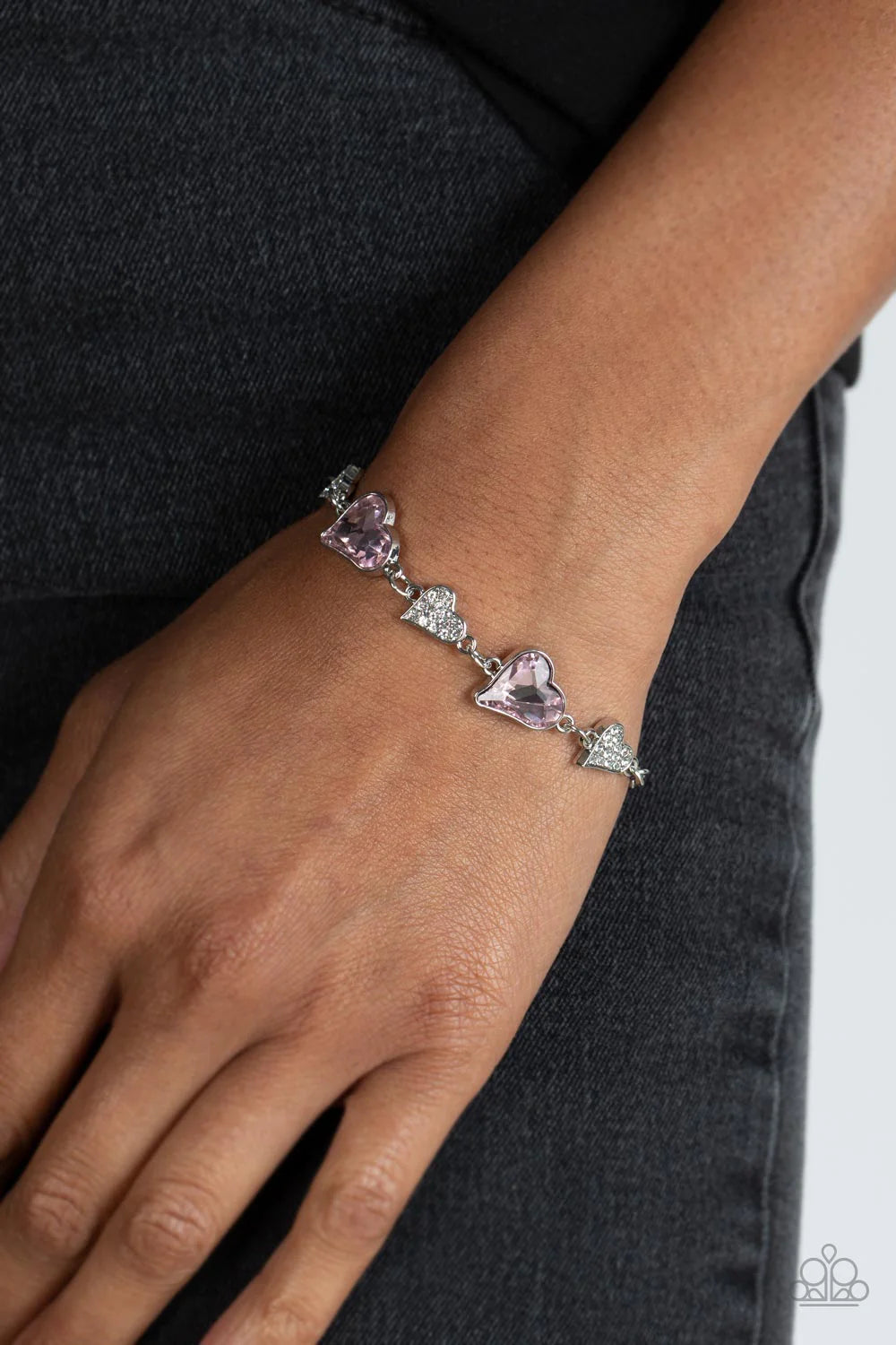 Paparazzi Accessories Cluelessly Crushing - Pink An asymmetrical collection of hearts coalesce around the wrist in this flirty centerpiece. Three of the silver hearts are encrusted with dainty white rhinestones, while the other two heart frames boast soft
