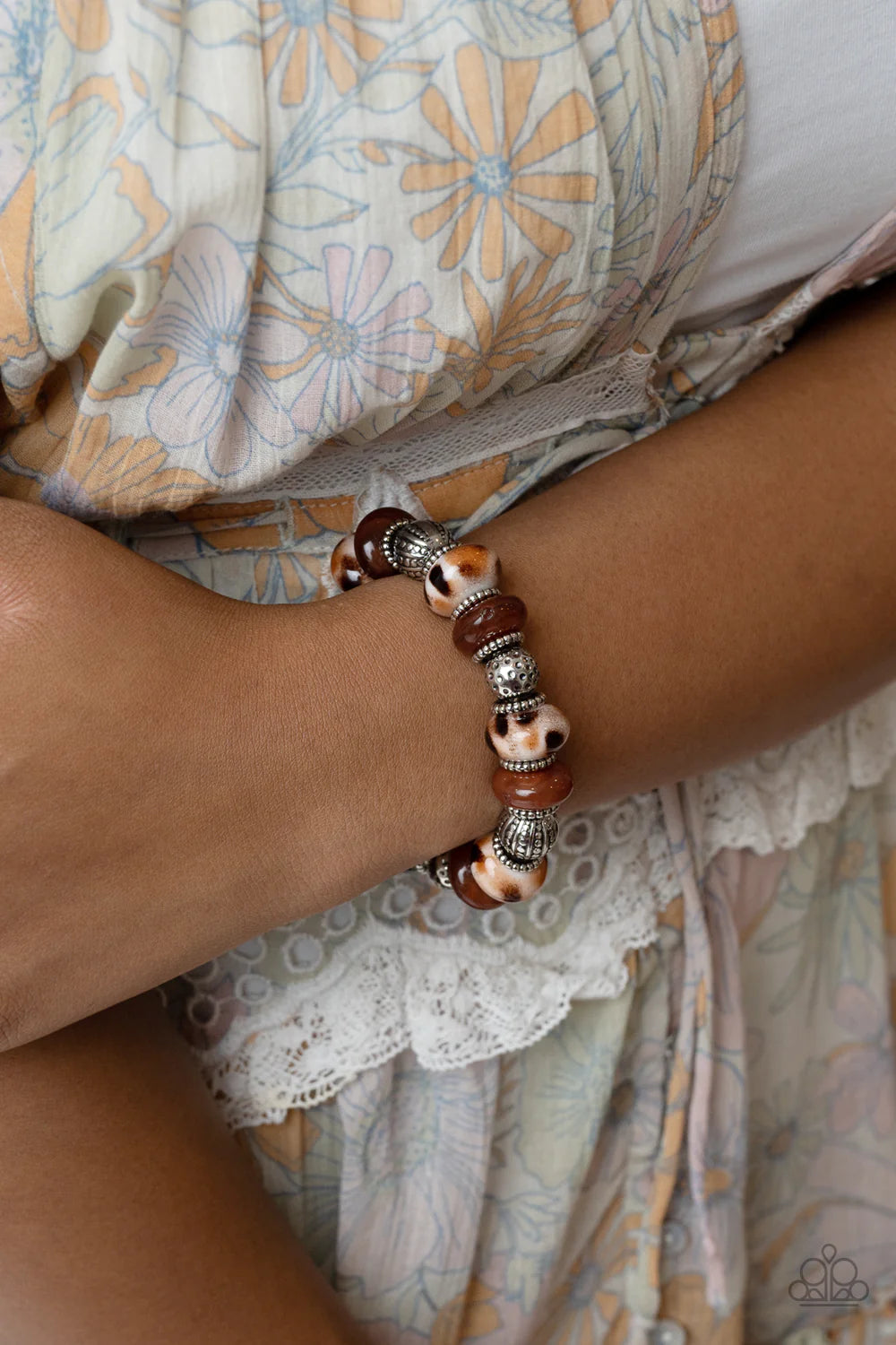 Paparazzi Accessories Warped Wayfarer - Brown An earthy collection of dotted silver beads, rounded milky Caramel Café beads, studded silver rings, brown-spotted ceramic-like beads and textured silver beads are threaded along an elastic stretchy band aroun