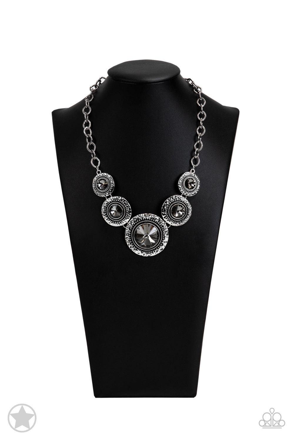 Paparazzi Accessories Global Glamour - Silver Gradually increasing in size, dramatically oversized smoky gems are pressed into the centers of hammered and silver studded frames. The blinding frames link below the collar for a glamorous, statement-making f