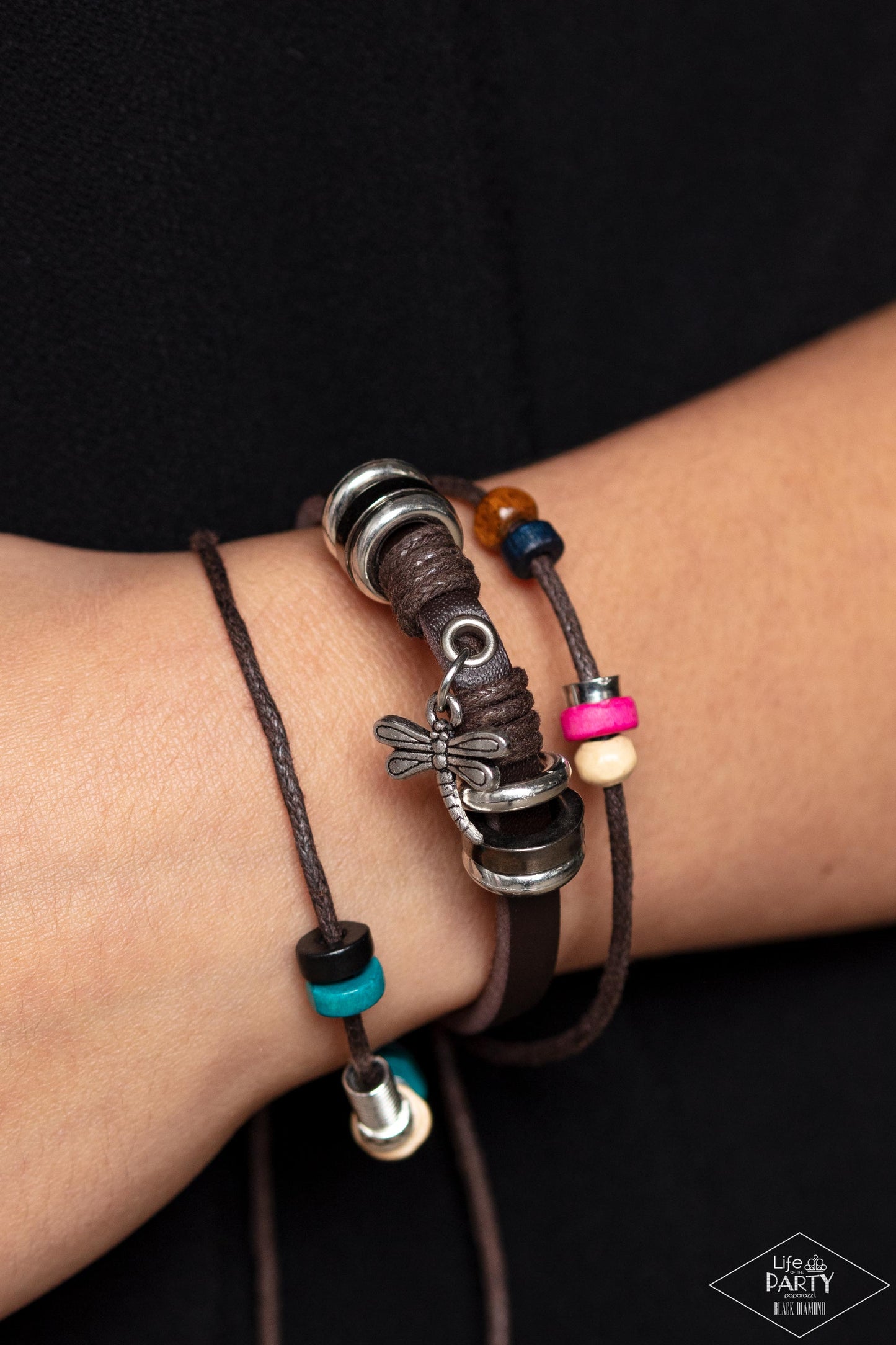 Paparazzi Accessories Fly High, Dragonfly - Brown Featuring colorful wooden beads, shiny metallic accents, and a shimmery dragonfly charm, mismatched strands of brown cording and leather layer across the wrist for a whimsical fashion. Features an adjustab