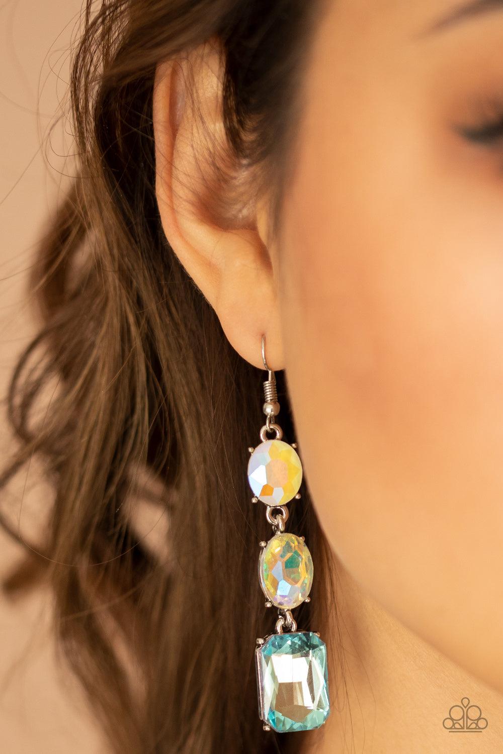 Paparazzi Accessories Dripping In Melodrama - Blue A blue emerald style gem swings from the bottom of a mismatched pair of iridescent and milky opalescent oval rhinestones, creating a stellar lure. Earring attaches to standard fishhook fitting. Sold as on