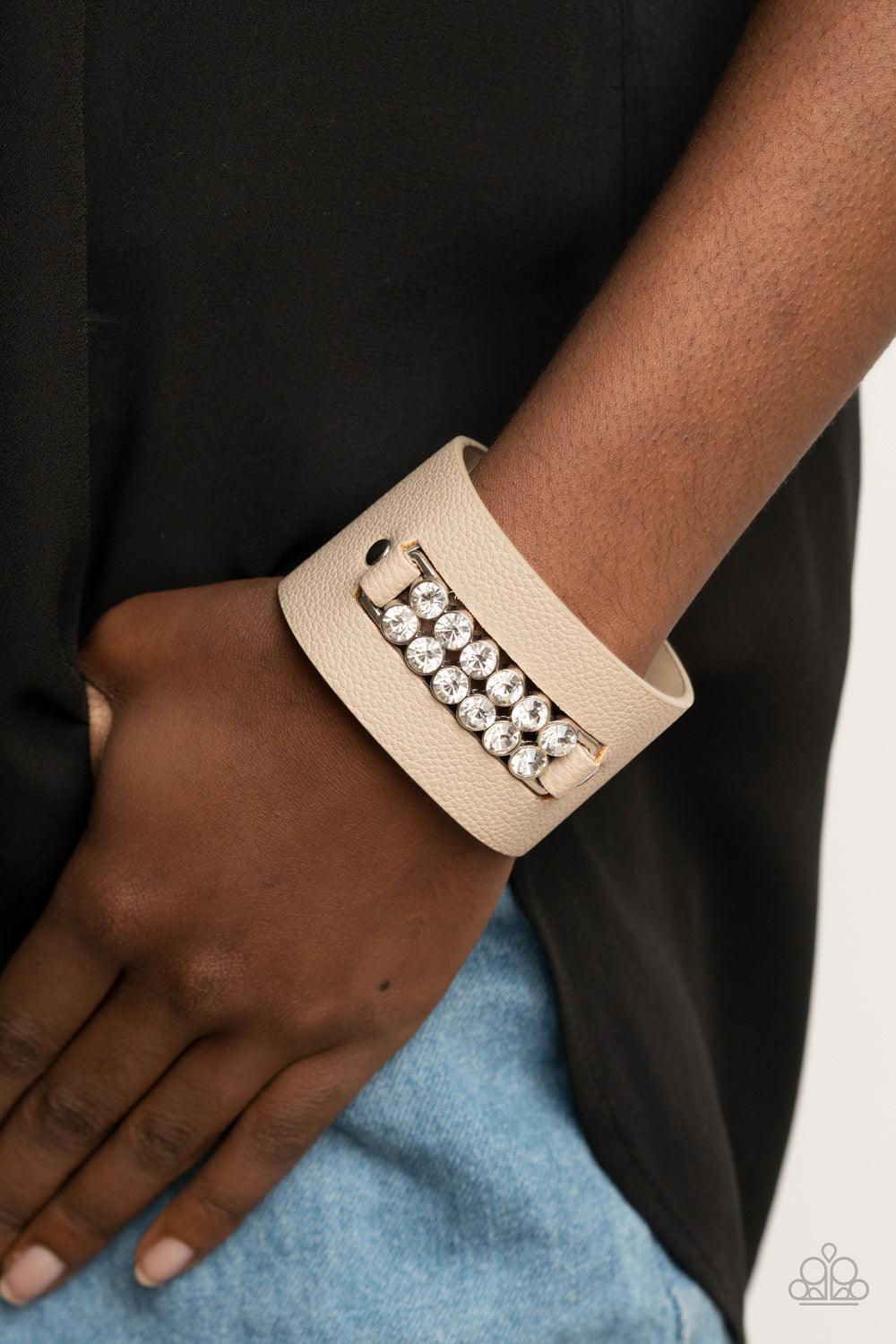 Paparazzi Accessories Runway Rebellion - Brown Two rows of oversized white rhinestones are studded in place across the center of a thick leather band, creating a sassy centerpiece around the wrist. Features an adjustable snap closure. Sold as one individu