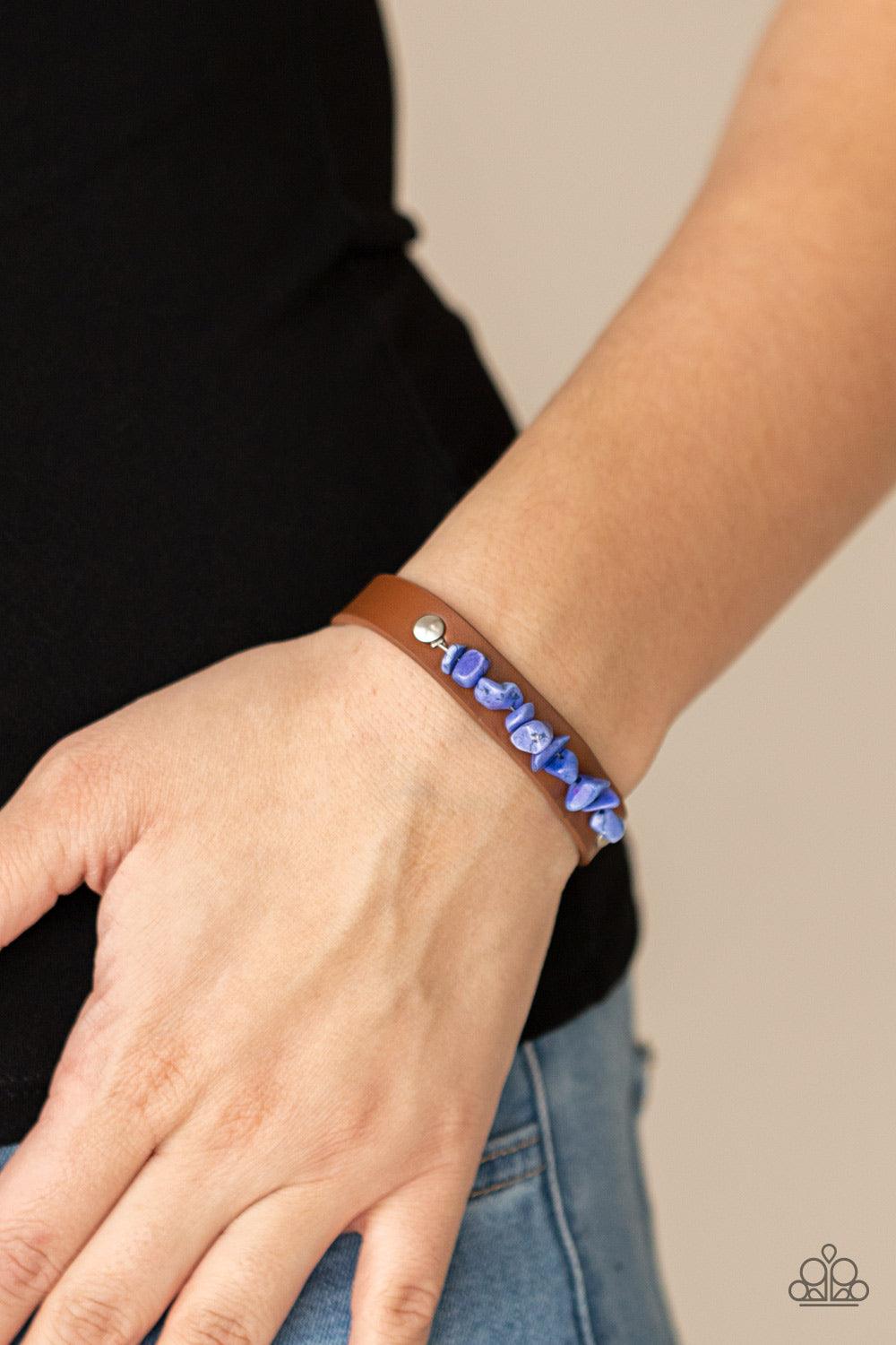 Paparazzi Accessories Pebble Paradise - Blue A strand of blue pebbles is studded in place across the front of a skinny brown leather band, creating a colorful earthy display around the wrist. Features an adjustable snap closure. Sold as one individual bra