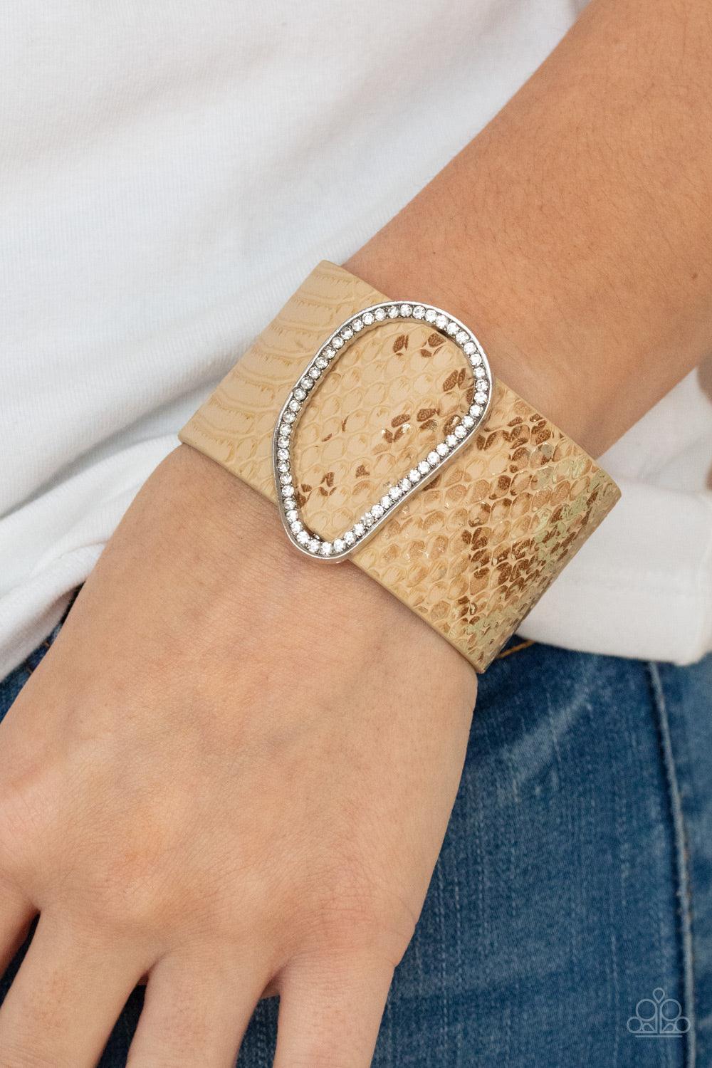 Paparazzi Accessories HISS-tory In The Making - Brown Encrusted with glassy white rhinestones, an asymmetrical silver fitting glides along a tan leather band adorned in a golden metallic python print for a wild look. Features an adjustable snap closure. S