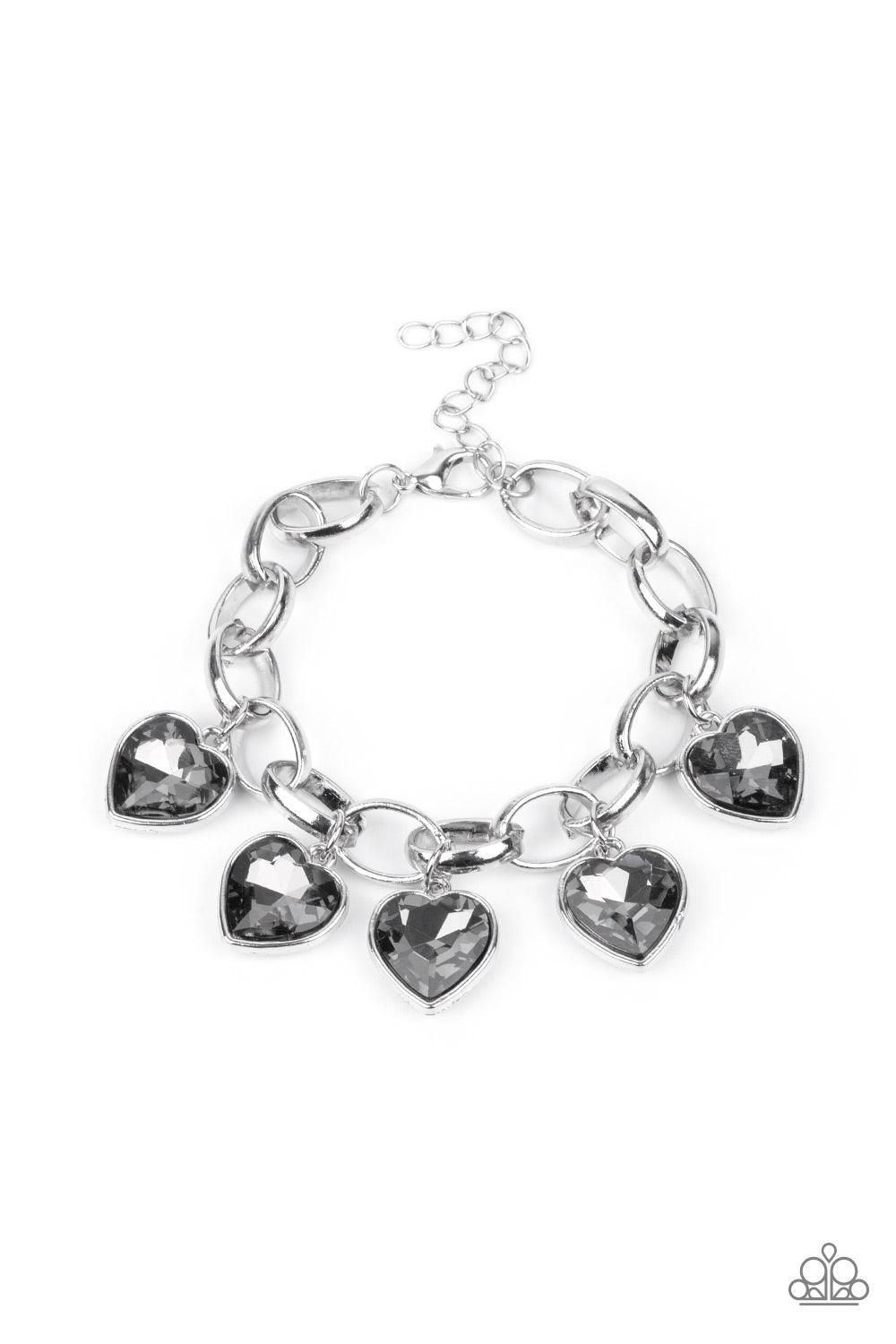 Paparazzi Accessories Candy Heart Charmer - Silver Smoky heart-shaped gems are encased in sleek silver frames that swing from an oversized silver chain, creating a sparkly fringe around the wrist. Features an adjustable clasp closure. Sold as one individu