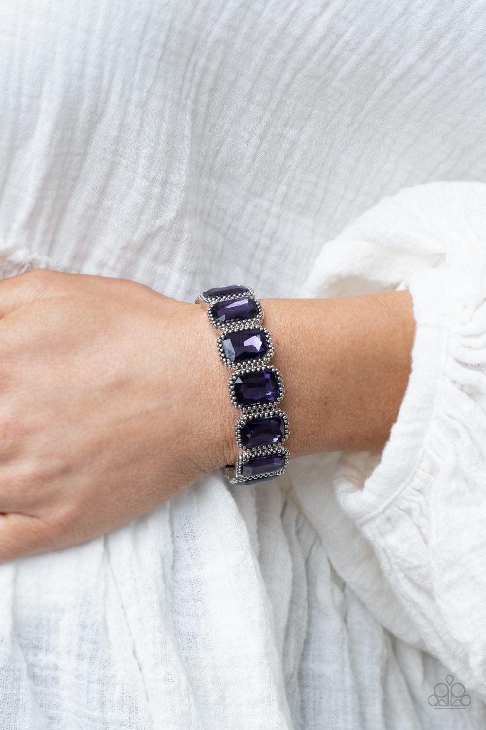 Paparazzi Accessories Studded Smolder - Purple Oversized emerald style purple gems are encased in antiqued studded frames that are threaded along stretchy bands around the wrist, creating a smoldering centerpiece. Sold as one individual bracelet. Jewelry