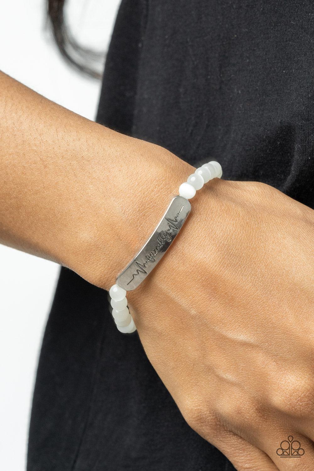 Paparazzi Accessories Family is Forever - White Stamped in heartbeats and the word, "Family," a shiny silver plate attaches to a strand of white cat's eye stone beads that are threaded along a stretchy band, creating a whimsically sentimental centerpiece
