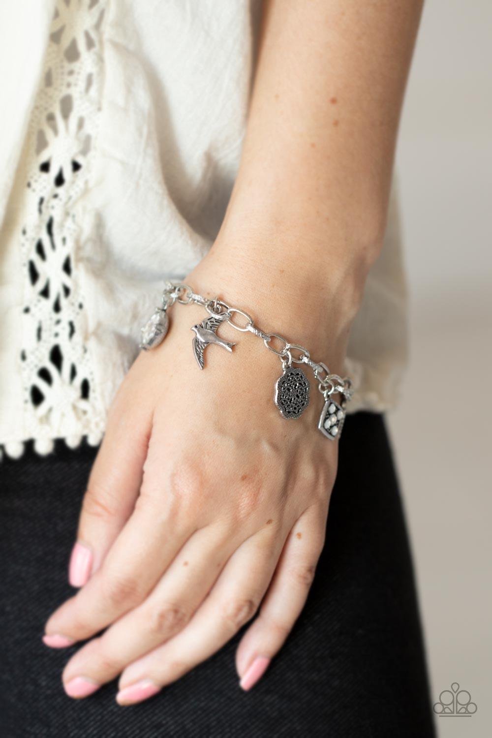 Paparazzi Accessories Fancifully Flighty - White White gems, a floral medallion, a bird in flight, and a fluttering feather coalesce into a whimsical charm bracelet as they dangle from a delicate silver chain around the wrist. Features an adjustable clasp