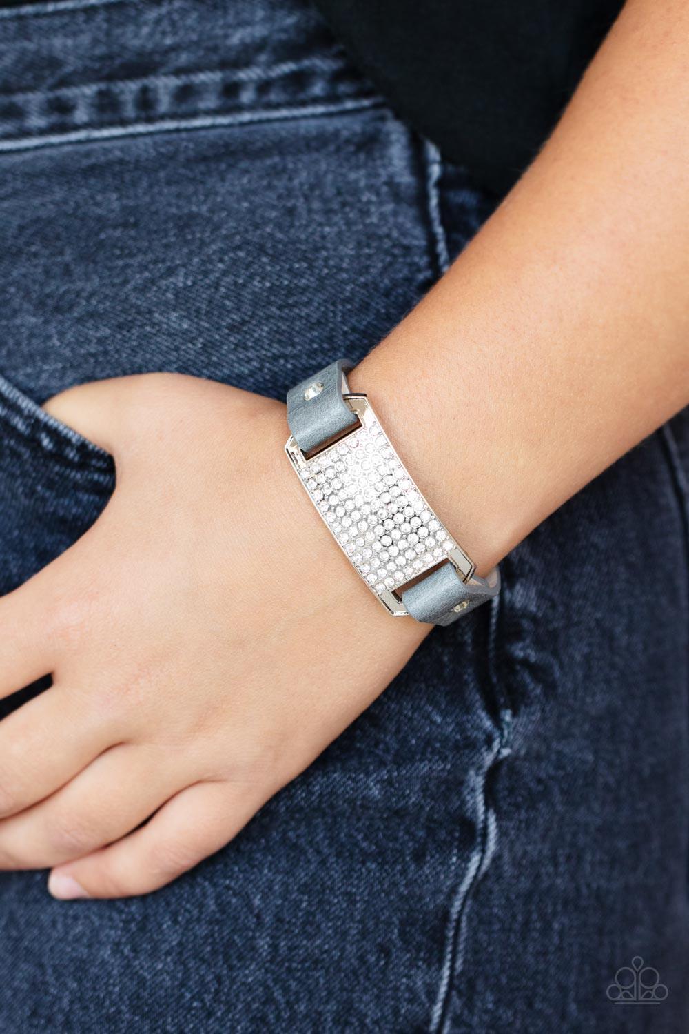 Paparazzi Accessories Urban Rivalry - Silver Gray leather bands are looped through the ends of a white rhinestone embellished silver frame and studded in place with glitzy white rhinestone studs, creating a glamorous centerpiece around the wrist. Features
