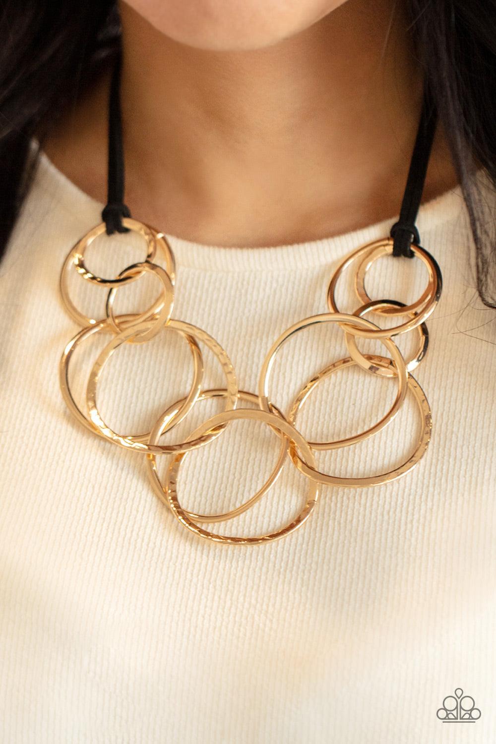 Paparazzi Accessories Spiraling Out of COUTURE - Gold Black suede cords knot around a mismatched assortment of hammered gold rings that interlock below the collar, creating two rows of dizzying texture. Features an adjustable clasp closure. Sold as one in
