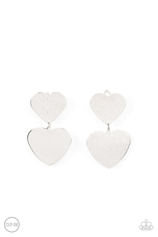 Paparazzi Accessories Cowgirl Crush - Silver *Clip-On Featuring a shimmery scratched finish, an oversized silver heart charm swings from the bottom of a smaller silver heart charm, resulting in a flirtatious lure. Earring attaches to a standard clip-on fi