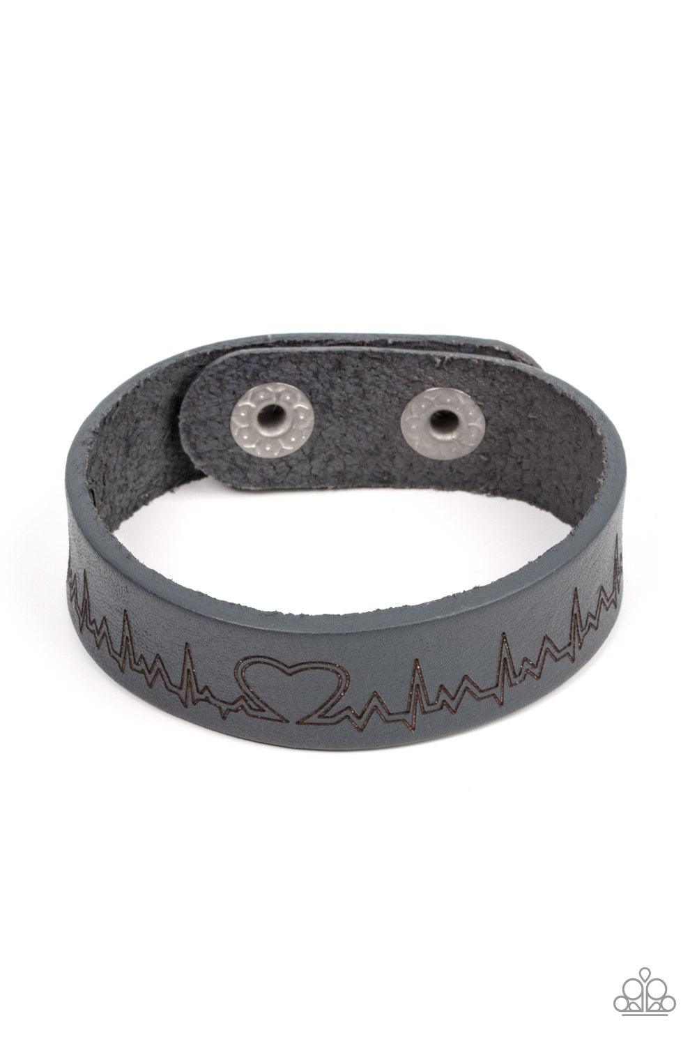 Paparazzi Accessories Haute Heartbeat - Silver Culminating into a heart at the center, a zigzagging pattern reminiscent of a heartbeat is etched across the front of a gray leather band around the wrist for a whimsical fashion. Features an adjustable snap