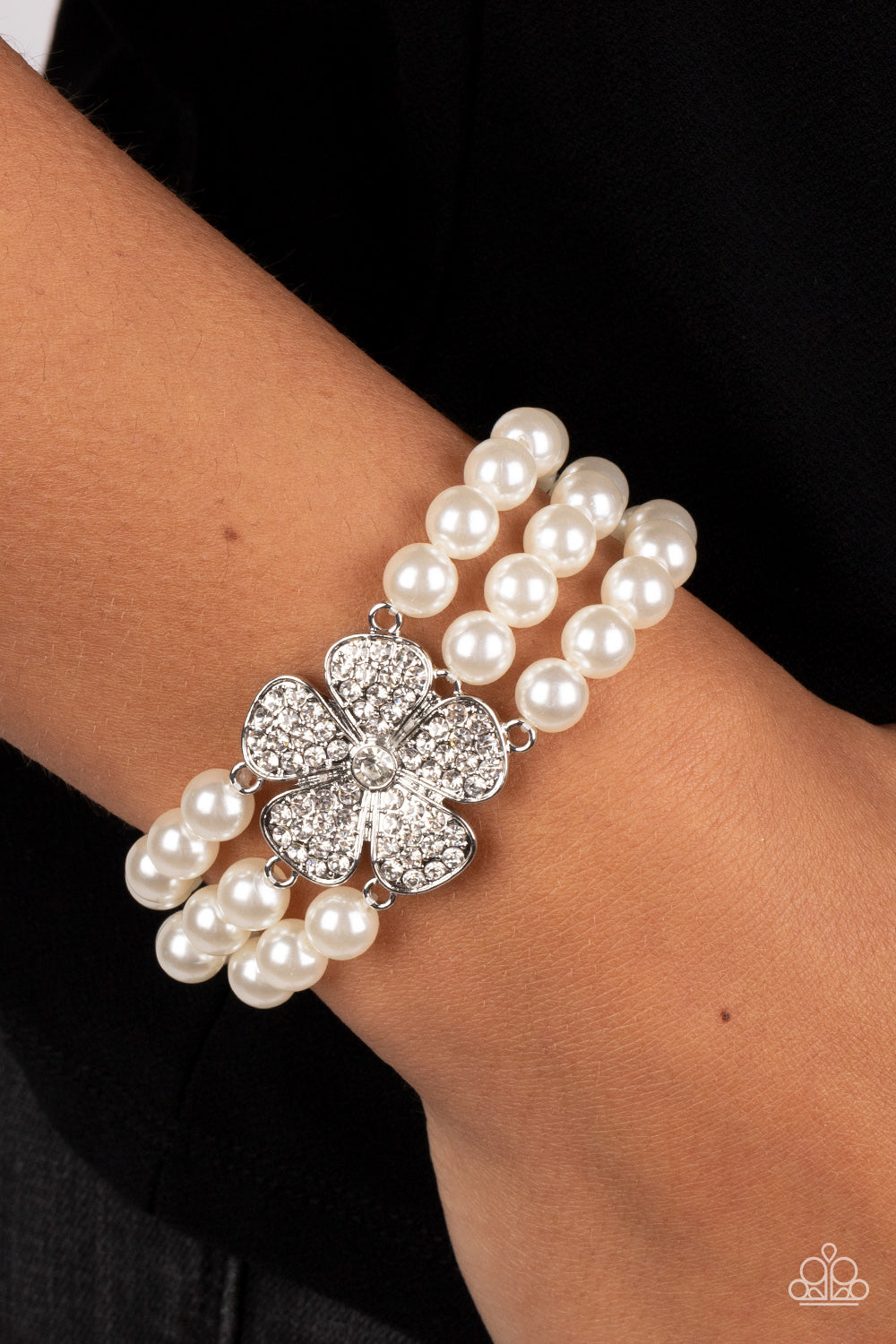 Paparazzi Accessories Park Avenue Orchard - White Separated by dainty silver plates, classic white pearls are threaded along three stretchy bands around the wrist. Encrusted in glassy white rhinestones, a glitzy silver flower blooms at the center of the w