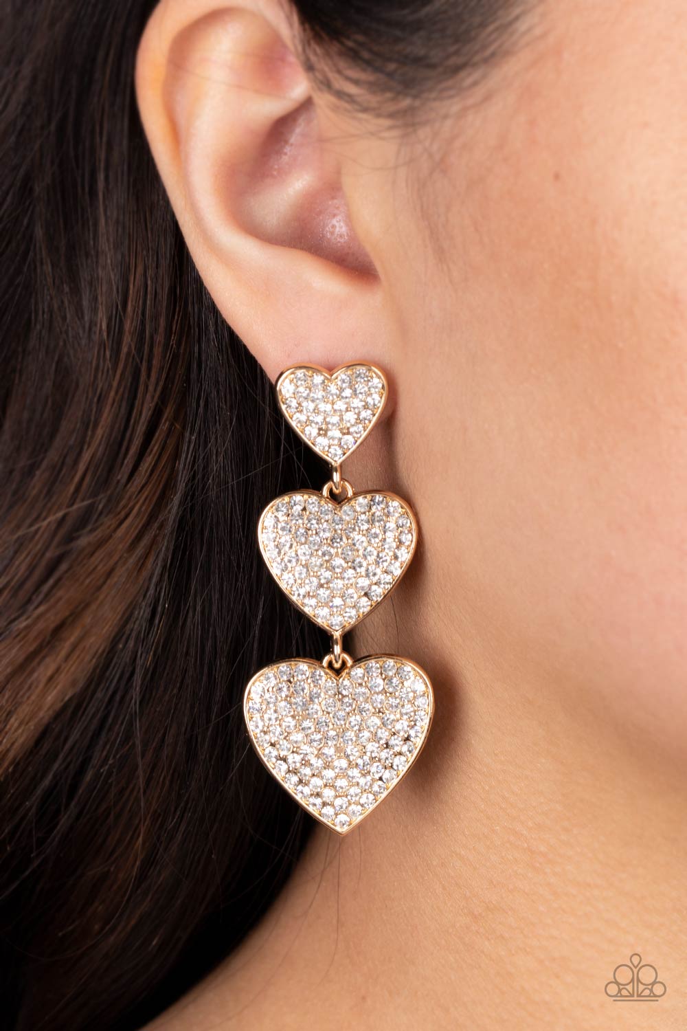 Paparazzi Accessories Couples Retreat - Gold Three white rhinestone-studded gold hearts gradually increase in size as they cascade down the ear in a shimmery display. Each of the hearts interconnect to one another adding a shifting, whimsical detail to th