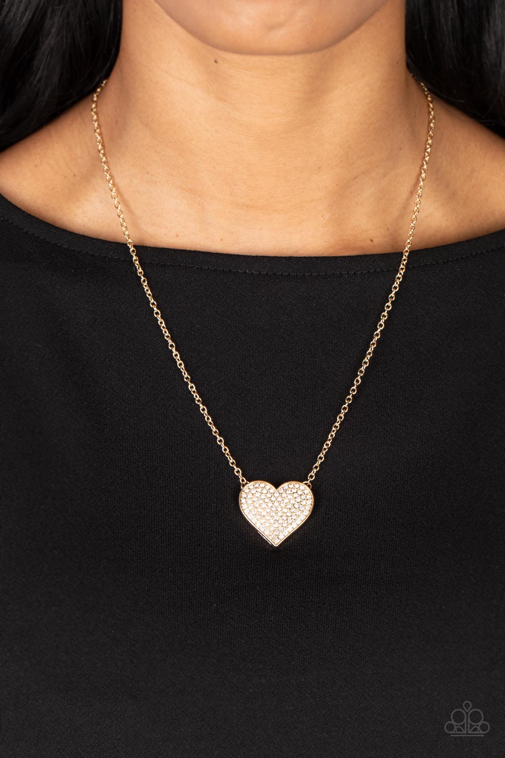 Paparazzi Accessories Spellbinding Sweetheart - Gold A heart-shaped pendant in a gold finish is anchored between two strands of delicate chain in the same reflective finish. The interior of the heart is filled with glittery white rhinestones, inviting onl