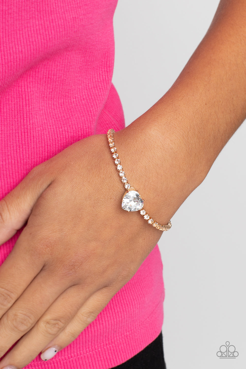 Paparazzi Accessories Bedazzled Beauty - Gold An oversized white heart-shaped gem, set in an airy, pronged gold fitting, glitters at the center of a blinding row of dainty, glassy white rhinestones set in square gold fittings, resulting in a flirtatious s