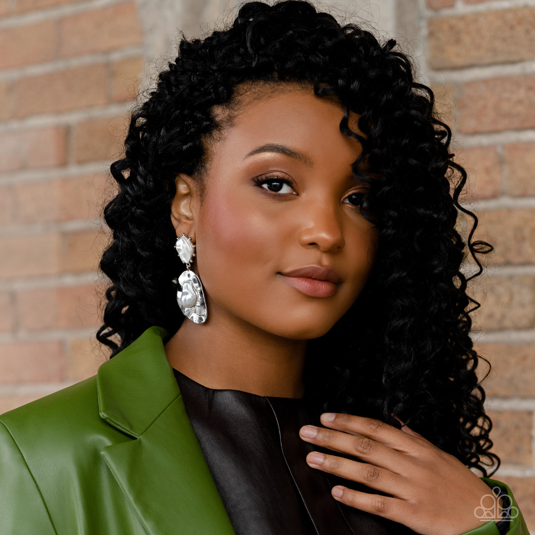 Paparazzi Accessories Rippling Rhapsody - White An oversized hammered, asymmetrical silver disc dangles from a more dainty, asymmetrical silver frame, accented with raised silver studs around its edges. Pressed in the center of the studded display, an abs