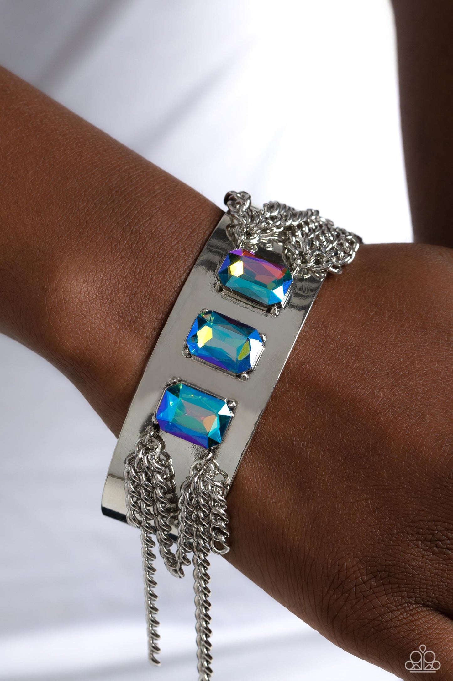 Paparazzi Accessories CHAIN Showers - Multi A thick, industrial silver cuff is topped by three brilliant UV-shimmery, emerald-cut gems. Strands of silver curb chain stream from each side of the trio of glitz, adding undeniable drama and eye-catching movem