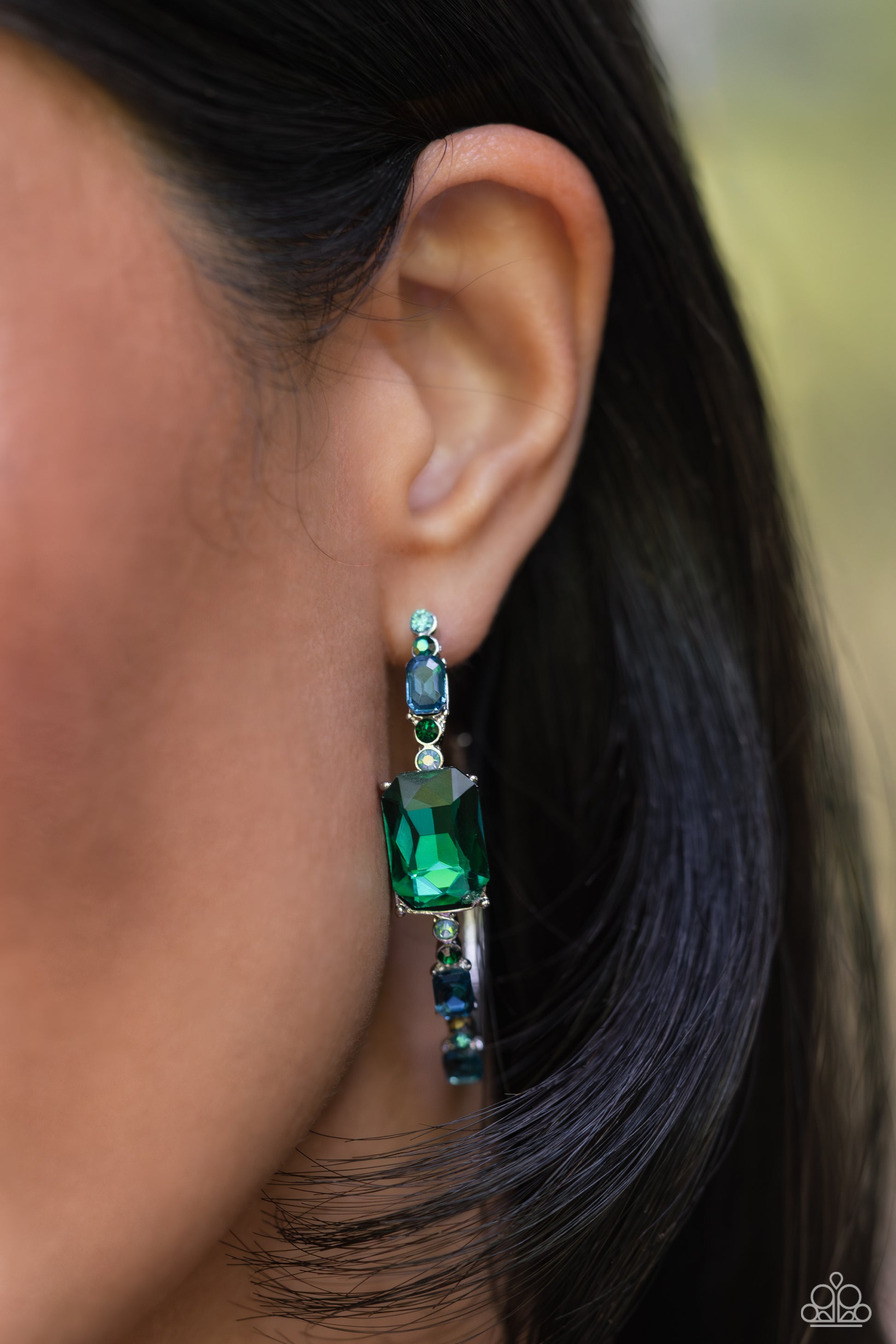 Paparazzi Accessories Elite Ensemble - Green Encrusted in round and emerald-cut aquamarine and emerald gems, some featuring an iridescent sheen, an exaggerated oblong silver hoop curls around the ear, refracting light in a dramatic, knockout finish. Earri
