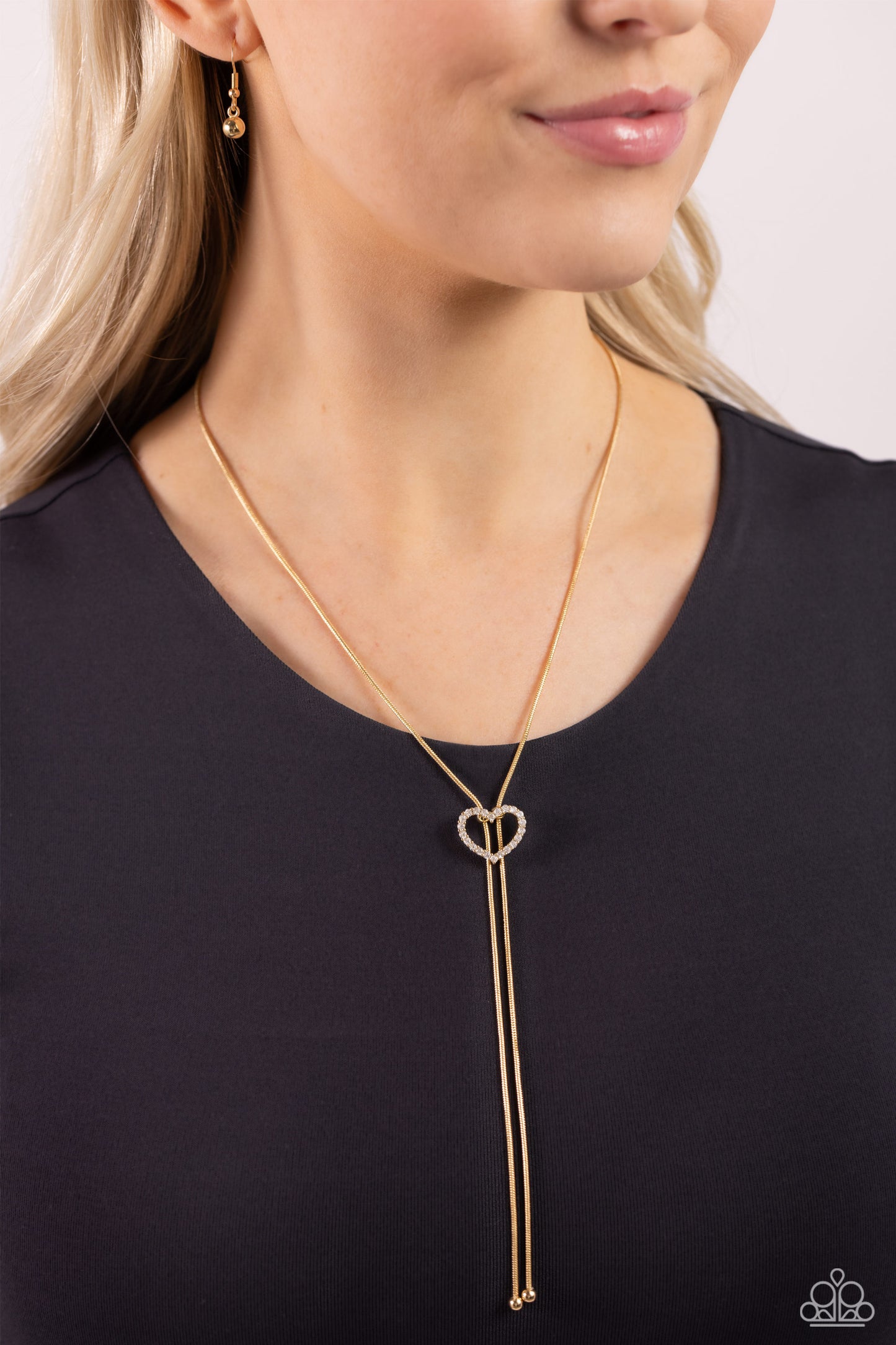Paparazzi Accessories Tempting Tassel - Gold A dainty white rhinestone-encrusted heart silhouette slides along dainty strands of glistening gold snake chain for a timeless, refined tassel. Features a bolo closure. Sold as one individual necklace. Includes