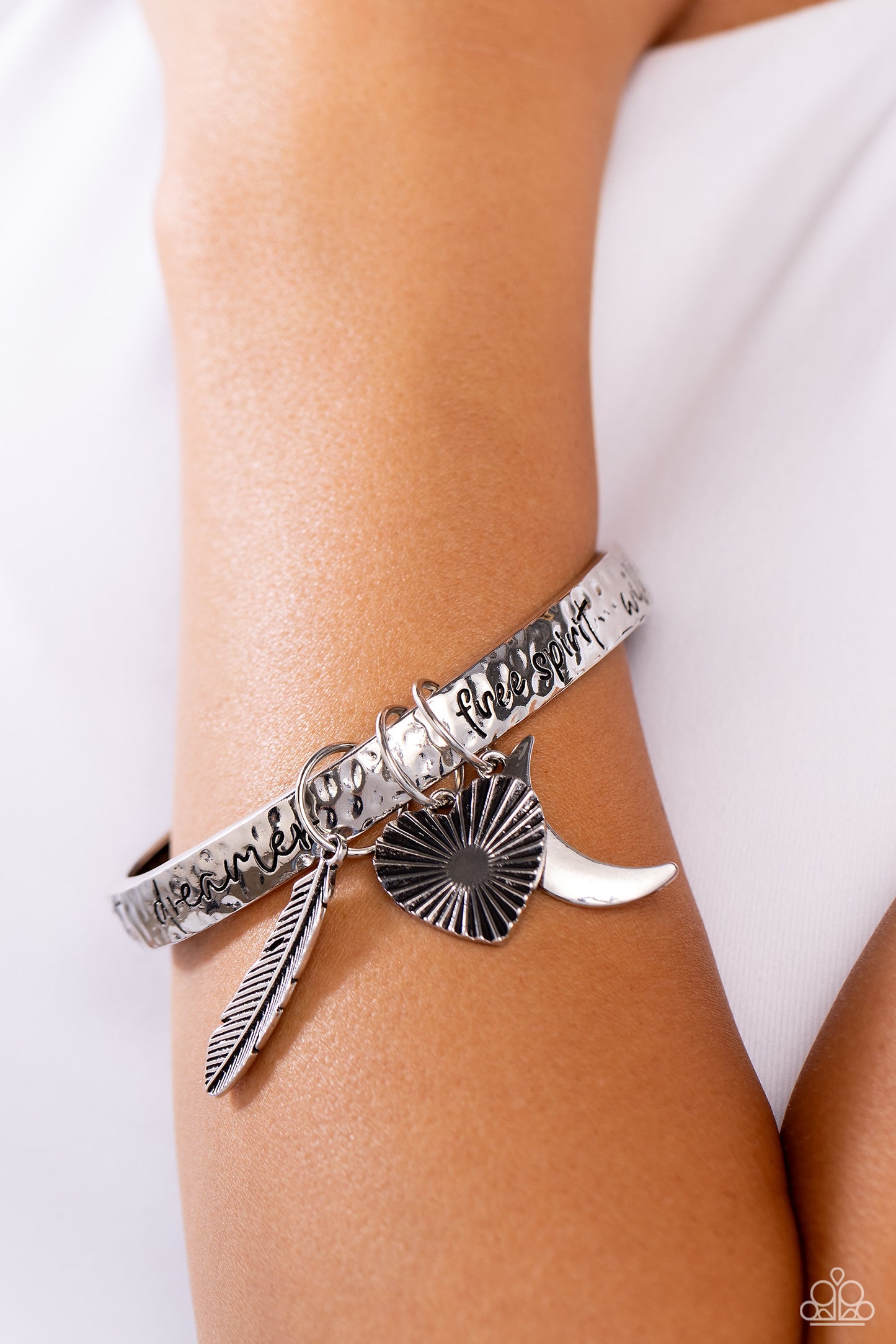 Paparazzi Accessories Free-Spirited Fantasy - Silver A hammered silver bangle featuring a textured feather, sleek crescent moon, and textured heart charms wraps around the wrist for an artisan-inspired fashion. Painted in a black hue, the phrases “free sp