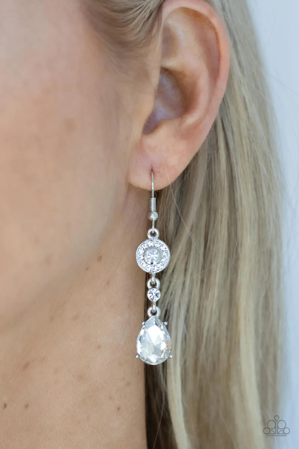 Paparazzi Accessories Graceful Glimmer - White A silver frame dotted in glassy white rhinestones, a solitaire white rhinestone, and an oversized white teardrop gem delicately link into a graceful lure. Earring attaches to a standard fishhook fitting. Sold