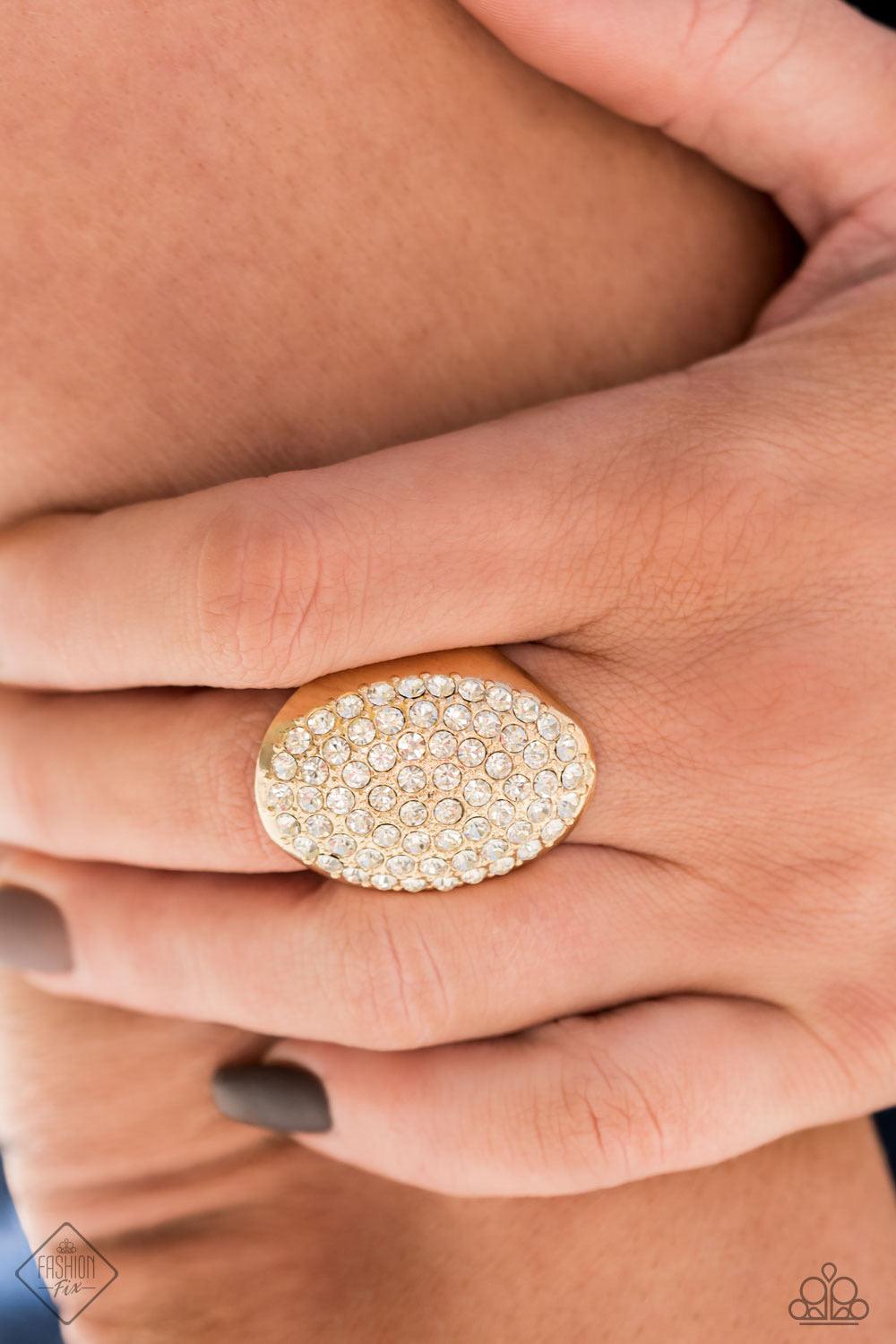 Paparazzi Accessories Test Your Luxe - Gold The front of a golden oval frame is haphazardly encrusted in a blinding scatter of glassy white rhinestones, creating a dramatic centerpiece atop the finger. Features a stretchy band for a flexible fit. Sold as