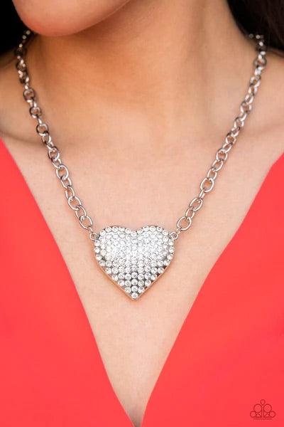 Paparazzi Accessories Heartbreakingly Blingy - White A dramatically oversized silver heart frame is encrusted in row after row of dazzling white rhinestones, resulting in heart-racing sparkle below the collar. Features an adjustable clasp closure. Sold as