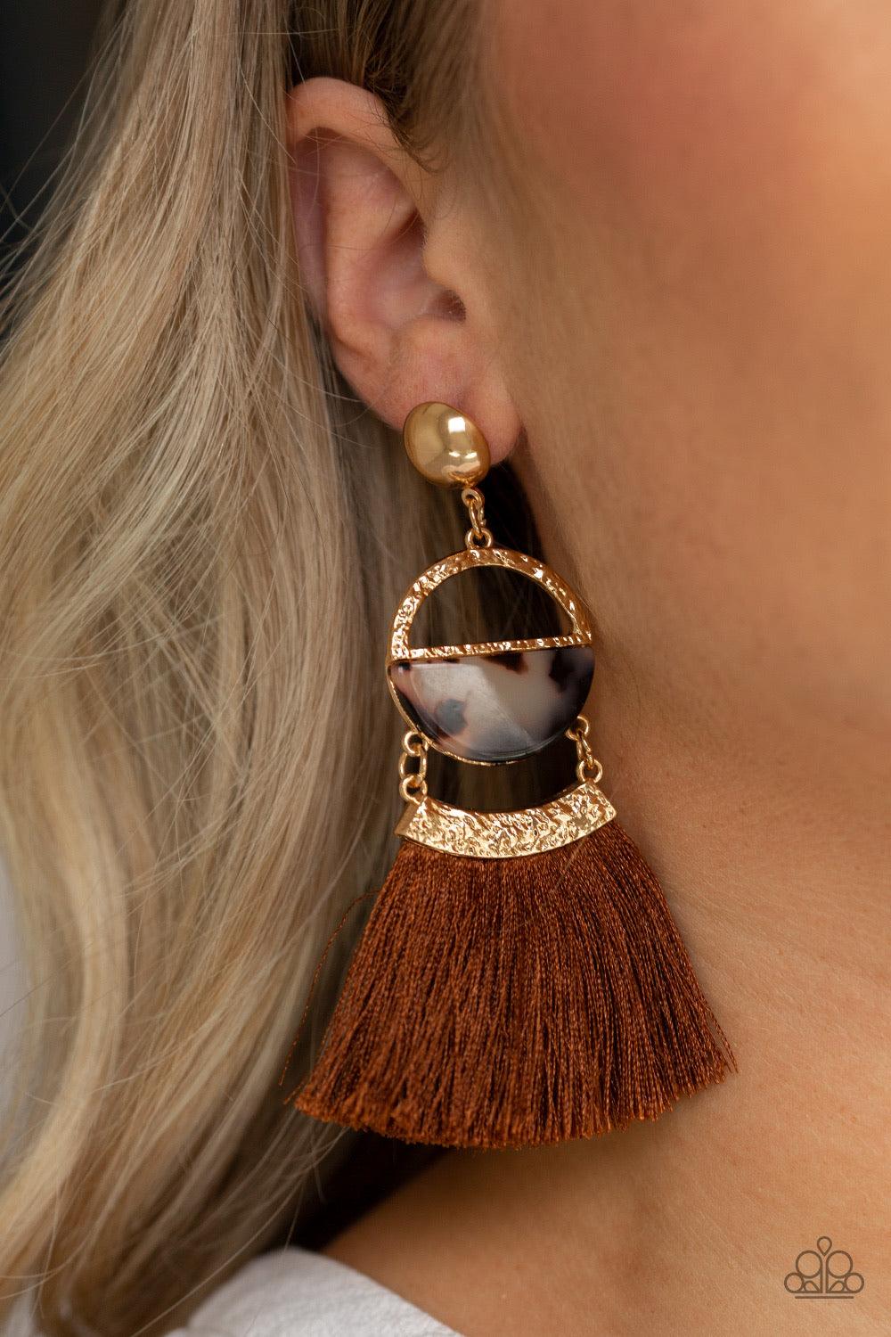 Paparazzi Accessories Tassel Trot - Brown A shimmery gold stud links with a hammered gold frame featuring a tortoiseshell print acrylic accent. Featuring a hammered gold fitting, a shiny brown threaded tassel attaches to the bottom of the retro lure for a