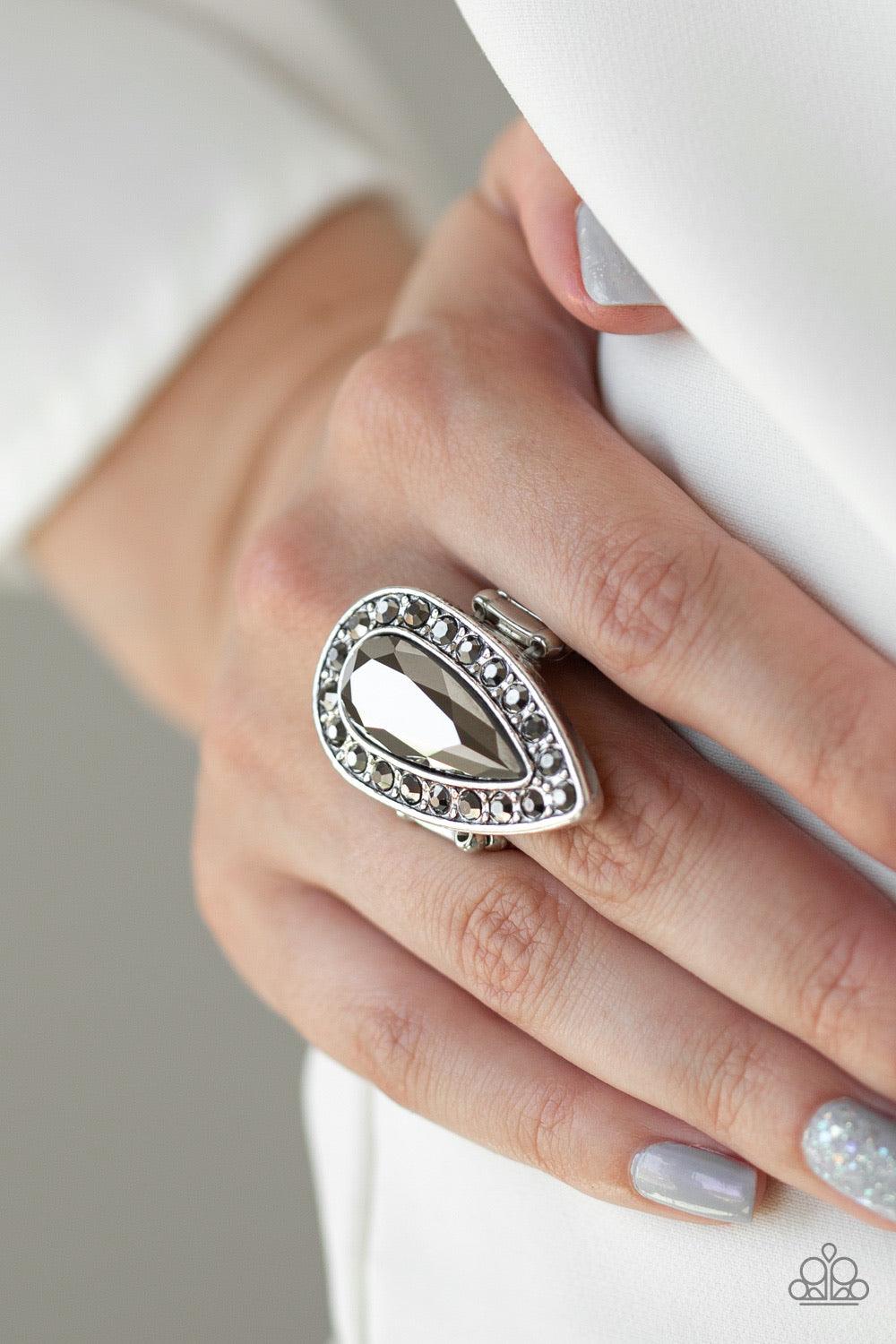 Paparazzi Accessories Majestic Mayhem - Silver An oversized hematite teardrop gem is pressed in the center of a glistening silver teardrop frame radiating with glittery hematite rhinestones for a fierce look. Features a stretchy band for a flexible fit. J