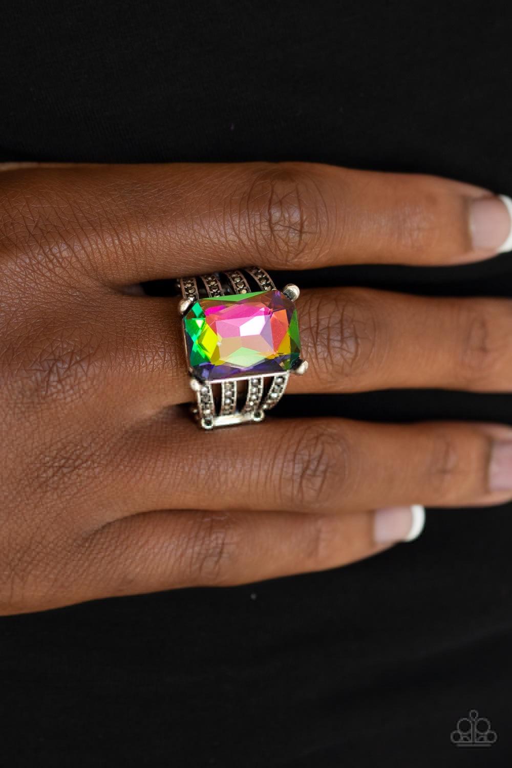 Paparazzi Accessories Expect Heavy REIGN - Multi Featuring a regal emerald style cut, an oversized rainbow gem is pressed into the center of stacked silver bands radiating with dainty hematite rhinestones for a dramatic look. Features a stretchy band for