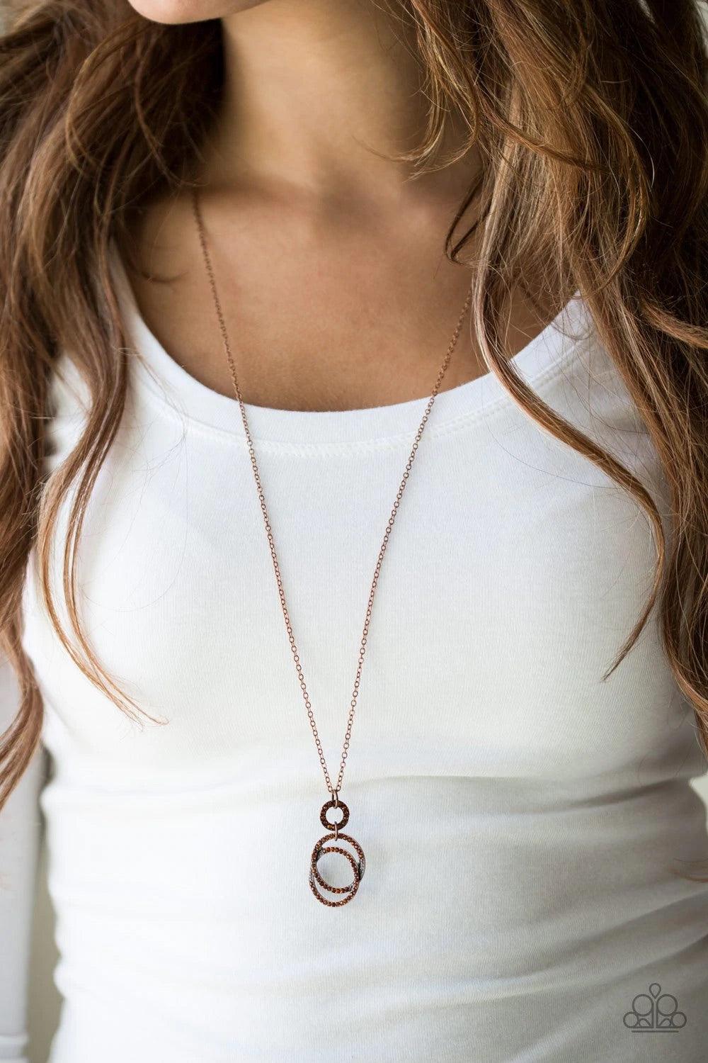 Paparazzi Accessories Timeless Trio - Brass Encrusted in radiant rhinestones, three copper hoops interlock at the bottom of an elongated copper chain for an elegant look. Features an adjustable clasp closure. Sold as one individual necklace. Includes one