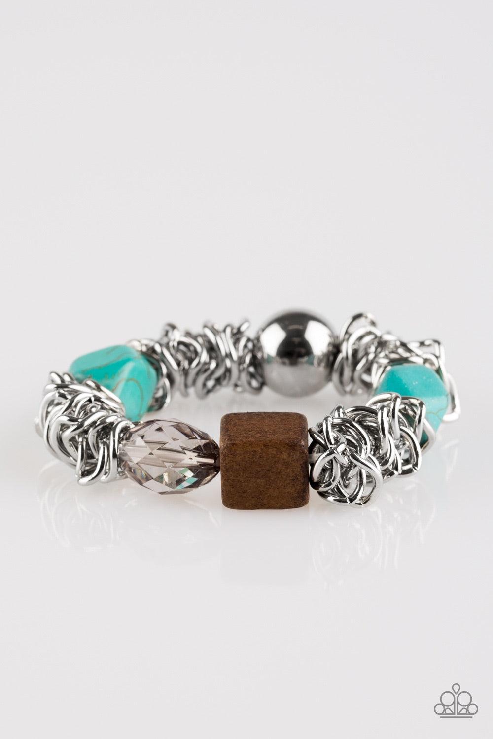 Paparazzi Accessories Mesmerizingly Magmatic - Blue A mishmash of bold silver chain, refreshing turquoise stones, a square wooden bead and metallic and crystal-like accents are threaded along a stretchy elastic band for a seasonal look. Jewelry