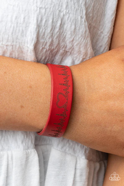 Paparazzi Accessories Haute Heartbeat - Red Culminating into a heart at the center, a zigzagging pattern reminiscent of a heartbeat is etched across the front of a red leather band around the wrist for a whimsical fashion. Features an adjustable snap clos