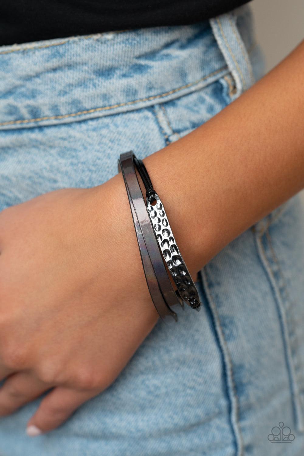 Paparazzi Accessories High-Strung Style - Black Shiny black cords and pieces of oil spill leather layer across the wrist. A hammered silver frame is knotted in place in the center, adding flashy hints of shimmer to the edgy centerpiece. Features a snap ma