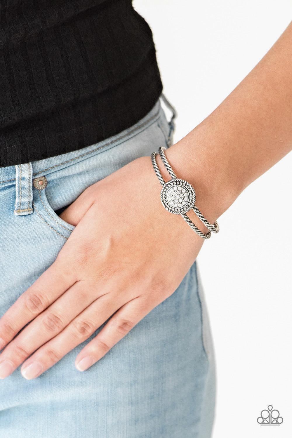 Paparazzi Accessories Definitely Dazzling - White Brushed in an antiqued shimmer, twisted silver bars arc across the finger, coalescing into an airy cuff. Radiating in silver studs and glittery white rhinestones, a round silver frame adorns the center for