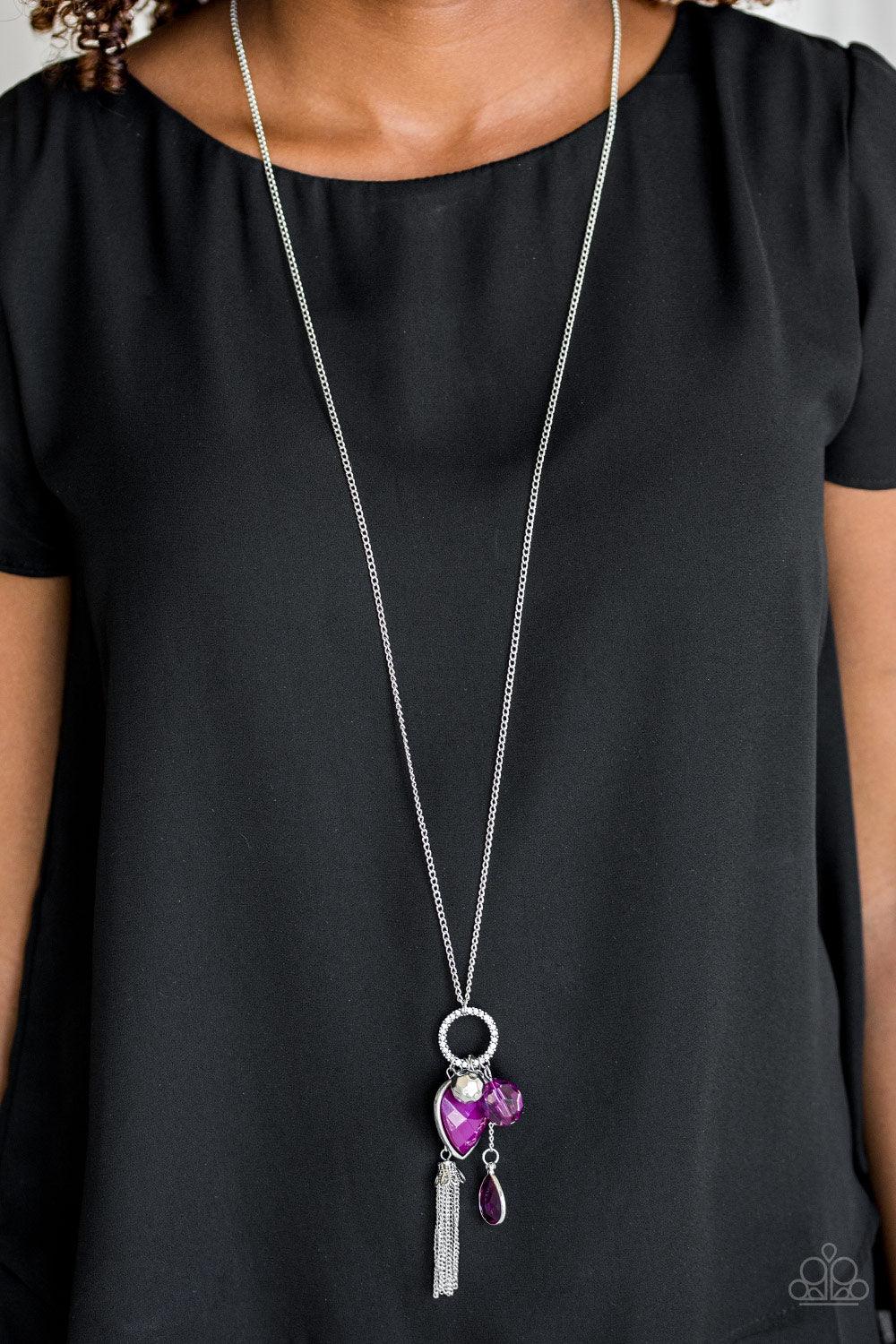 Paparazzi Accessories Haute Heartbreaker - Purple Infused with a lengthened silver chain, an array of glassy purple and shimmery silver accents swing from the bottom of a white rhinestone encrusted frame. A faceted purple heart frame swings from the botto