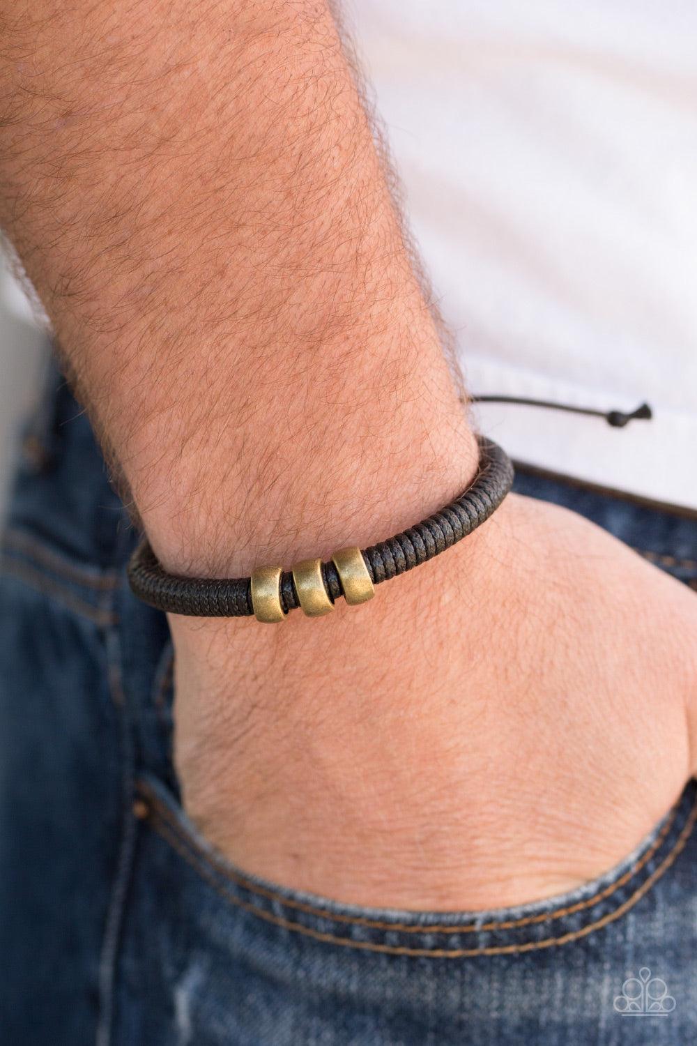 Paparazzi Accessories One For The Trail - Black Shiny black twine wraps around a black cord, creating an urban look around the wrist. Shiny brass beads slide along the cording for a rugged finish. Features an adjustable sliding knot closure. Jewelry
