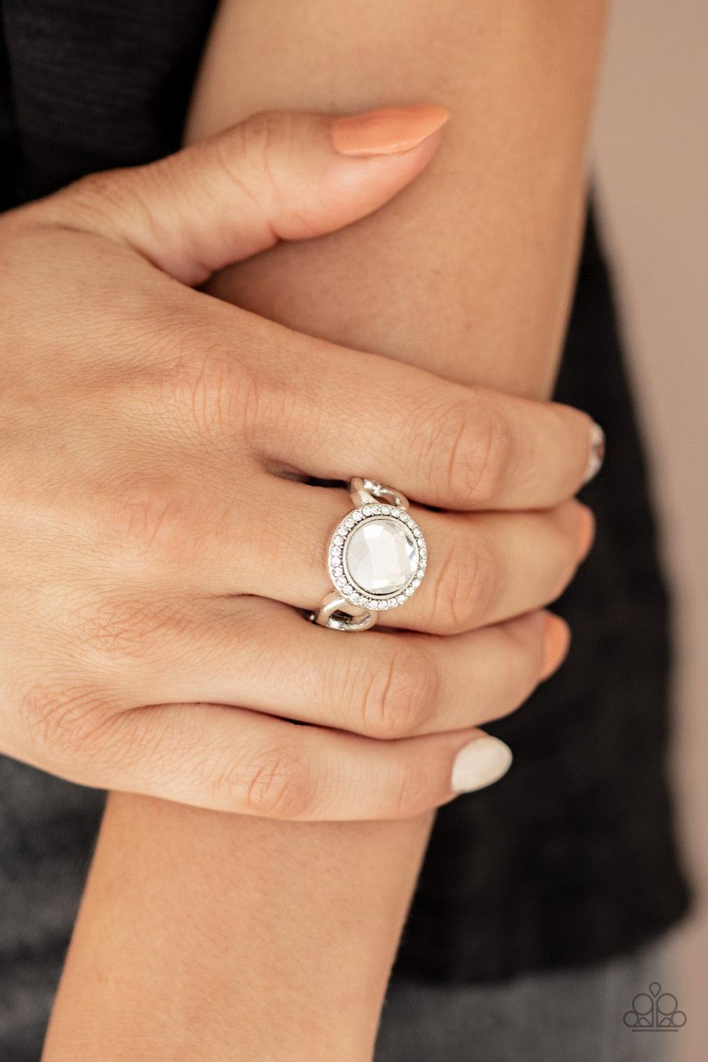 Paparazzi Accessories It’s Gonna Glow! - White An oversized white gem is pressed into the center of a round silver frame encrusted in a ring of radiant white rhinestones for a regal flair. Features a dainty stretchy band for a flexible fit. Sold as one in