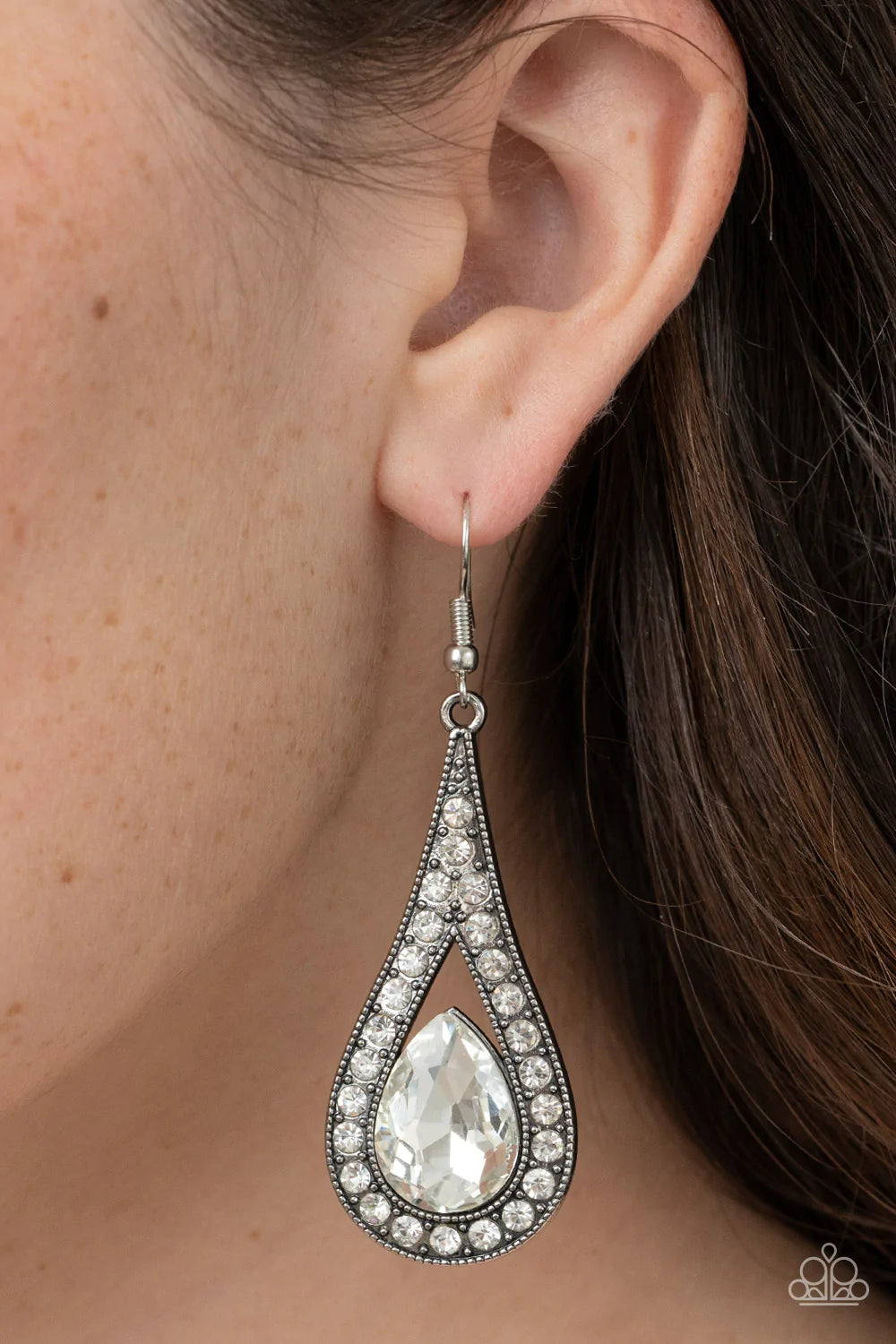 Paparazzi Accessories A-Lister Attitude - White An oversized white teardrop gem is nestled inside the bottom of a ribbon of glittery white rhinestones, creating a dramatic lure. Earring attaches to a standard fishhook fitting. Sold as one pair of earrings