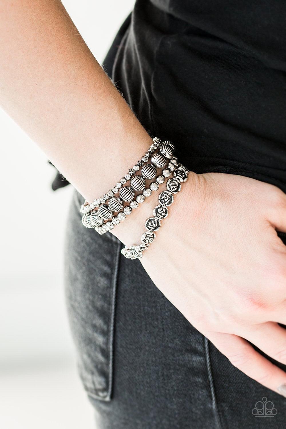 Paparazzi Accessories Rose Garden Gala -Silver A collection of silver roses, ornate silver beads, and dainty silver accents are threaded along stretchy bands, creating whimsical layers around the wrist.