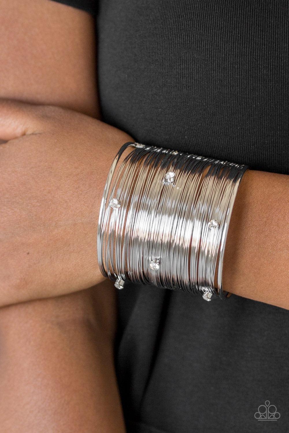 Paparazzi Accessories Professional Prima Donna - White Shimmery silver wires wrap back and forth along a silver frame, creating a bold cuff. Glassy white rhinestones are sprinkled across the dramatic cuff for a glamorous finish. Jewelry