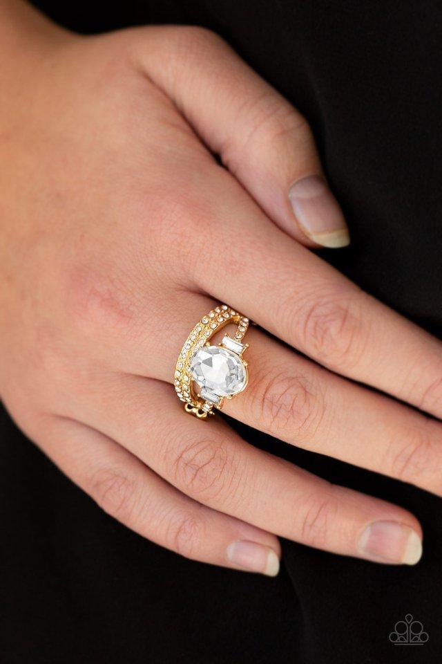 Paparazzi Accessories Bling Queen - Gold Paparazzi Bling Queen - Gold - Encrusted in glassy white rhinestones, shiny gold bands arc across the finger. Infused with emerald style rhinestones, an oversized white rhinestone crowns the layered bands for a reg