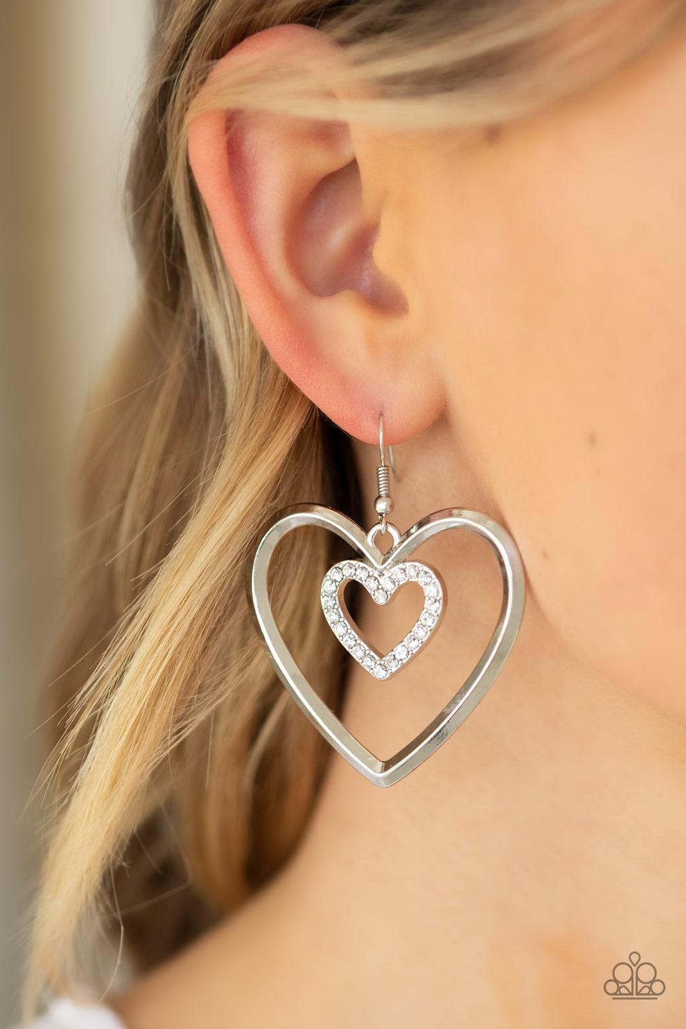 Paparazzi Accessories Heart Candy Couture - Silver A dainty white rhinestone encrusted heart frame swings from the top of an oversized silver heart frame, creating a charming duo. Earring attaches to a standard fishhook fitting. Jewelry