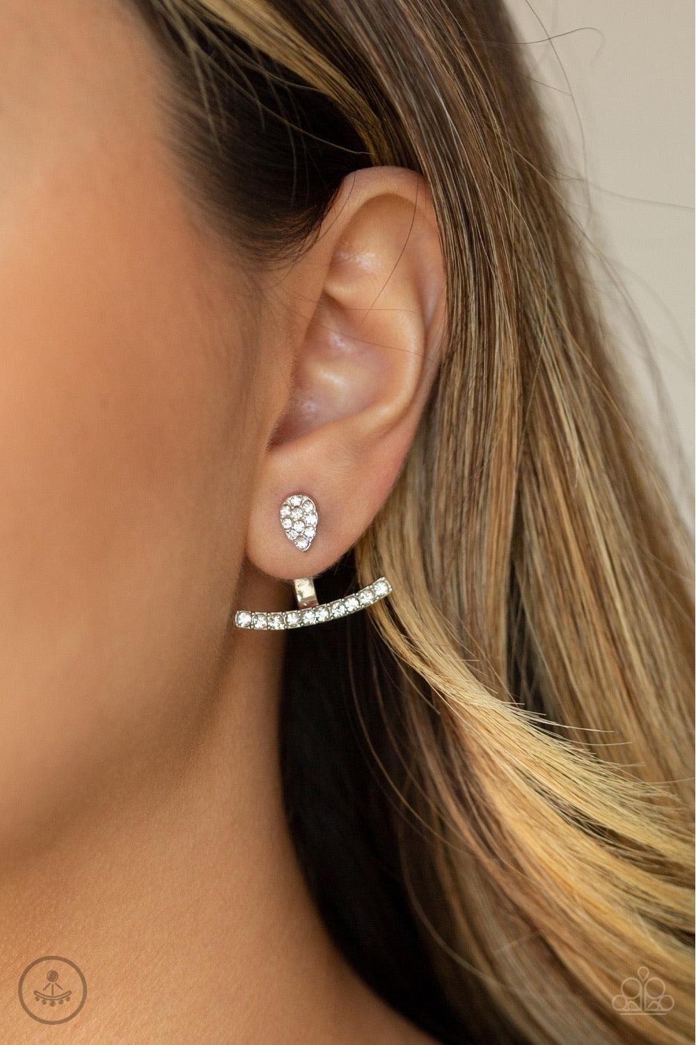 Paparazzi Accessories Glow Glimmer - White Encrusted in glassy white rhinestones, a dainty silver teardrop attaches to a double-sided post, designed to fasten behind the ear. Radiating with a row of glassy white rhinestones, a bowing silver frame peeks ou