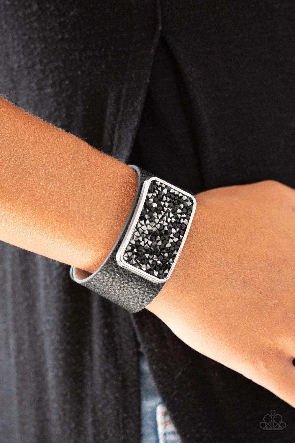 Paparazzi Accessories Interstellar Shimmer - Black A collision of black and hematite rhinestones collect inside a silver rectangular frame that is studded in place in the center of a thick black leather band, creating a sparkling statement piece around th