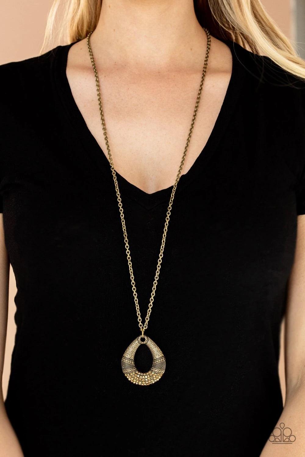 Paparazzi Accessories Glitz and Grind - Brass Studded and embossed in bands of texture, the bottom of a hammered brass teardrop is encrusted in golden topaz rhinestones, creating a glitzy pendant at the bottom of a lengthened brass chain. Features an adju